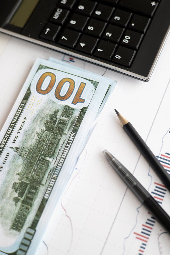 Stack of hundred dollar bills beside calculator and graph for financial analysis