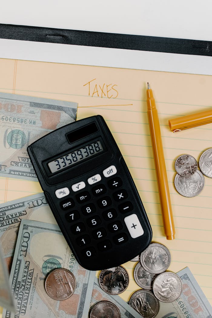 A financial planning setup with calculator, cash, and coins on a notepad labeled 'Taxes.'